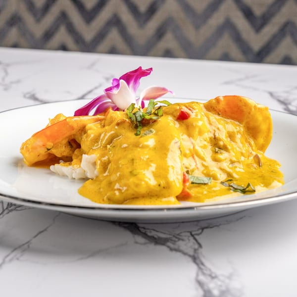Shrimp with yellow curry sauce and rice, garnished with a purple orchid and basil.