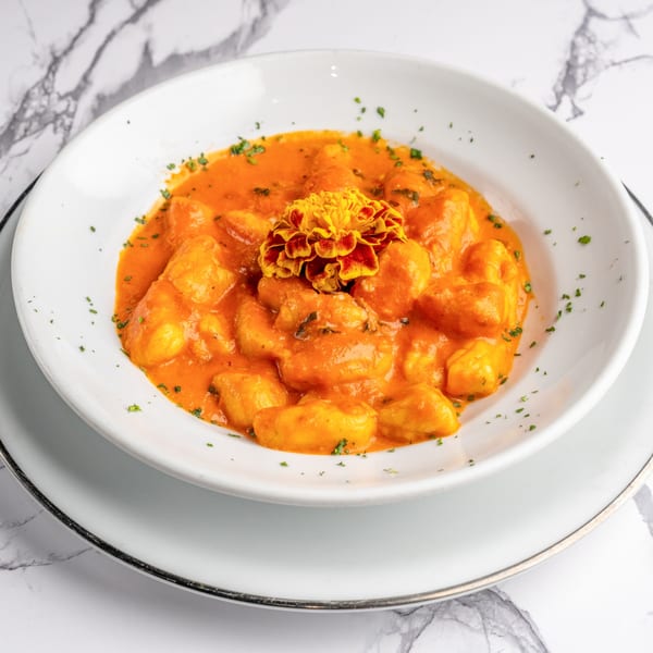 Italian gnocchi in a rich orange sauce, garnished with parsley and a vibrant marigold flower.