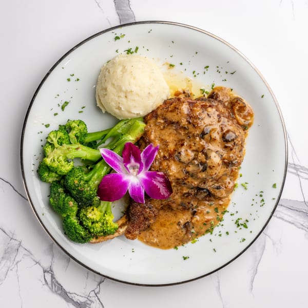 Chicken Marsala with mashed potatoes, broccoli, and a purple orchid garnish on a white plate.