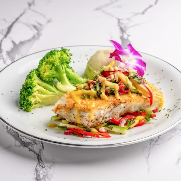 Pan-seared fish with mango salsa, broccoli, and mashed potatoes, garnished with an orchid.