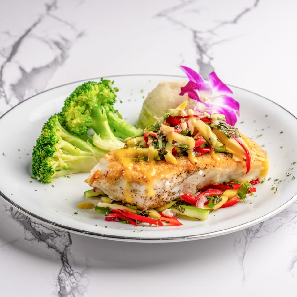 Pan-seared fish with mango salsa, broccoli, and mashed potatoes, garnished with an orchid.