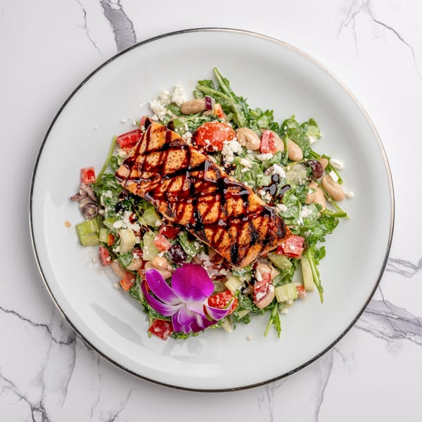 Grilled salmon with balsamic glaze on a fresh salad with feta, beans, and a purple orchid.