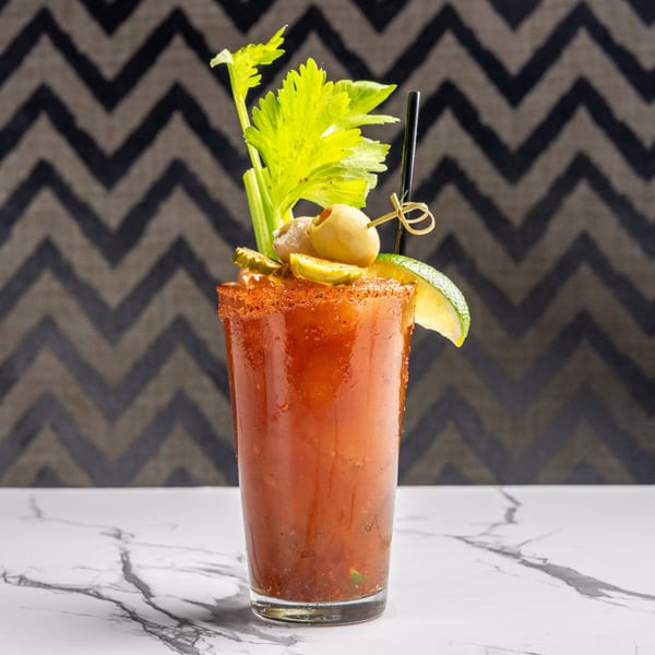 A Bloody Mary cocktail with celery, olives, pickles, and a lime wedge on a marble surface.