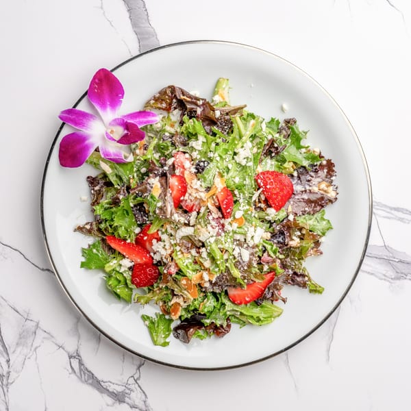 Fresh green and red lettuce salad with strawberries, feta cheese, and nuts, garnished with an orchid.