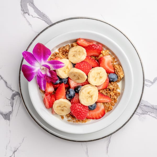 Overhead view of a granola bowl with fresh strawberries, blueberries, raspberries, and banana slices.