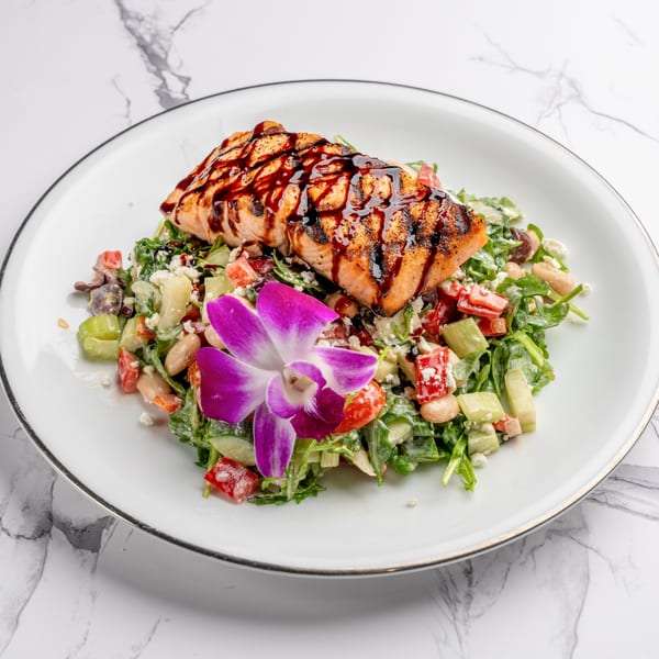 Grilled salmon with balsamic glaze on a fresh salad with a purple orchid garnish.
