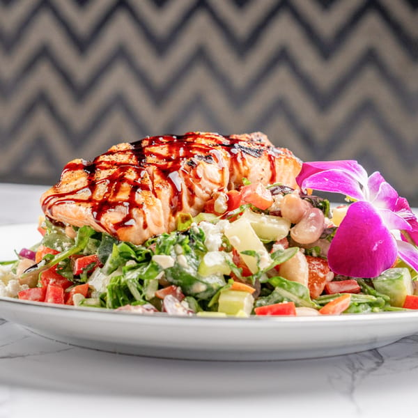 Grilled salmon with balsamic glaze on a fresh salad with feta, beans, and a purple orchid.