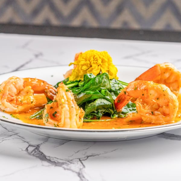 Shrimp scampi with sautéed spinach and a yellow flower garnish on a white plate.