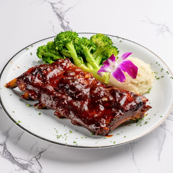 Ribs with BBQ sauce, mashed potatoes, broccoli, and a purple orchid on a white plate.