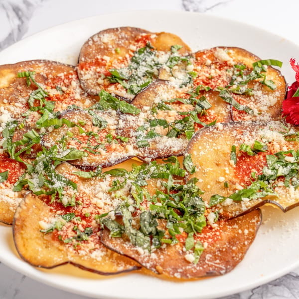 Fried eggplant slices topped with red sauce, grated cheese, and fresh basil on a white plate.