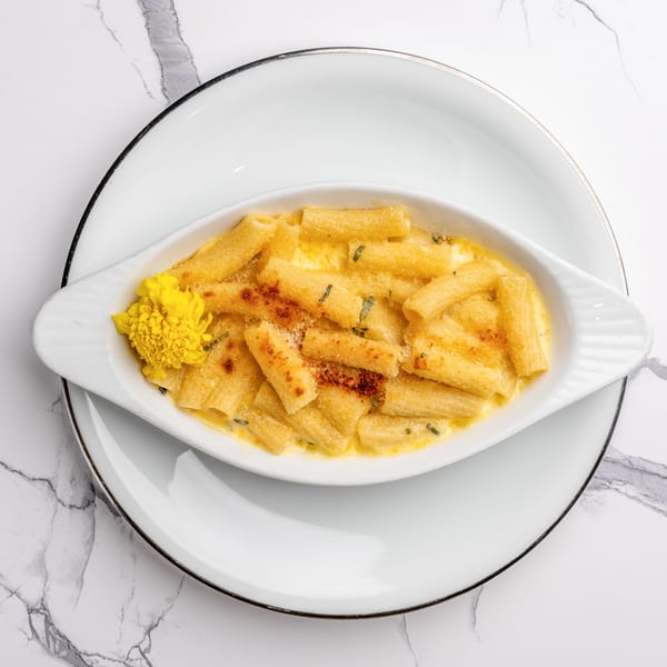 Baked rigatoni pasta with a creamy sauce, topped with breadcrumbs and a yellow flower garnish.