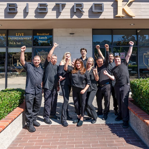 The Bistro K staff, dressed in black, pose cheerfully with raised fists outside the restaurant.