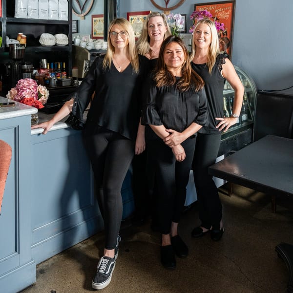 Four smiling women in black shirts and pants stand together inside The Bistro K restaurant.