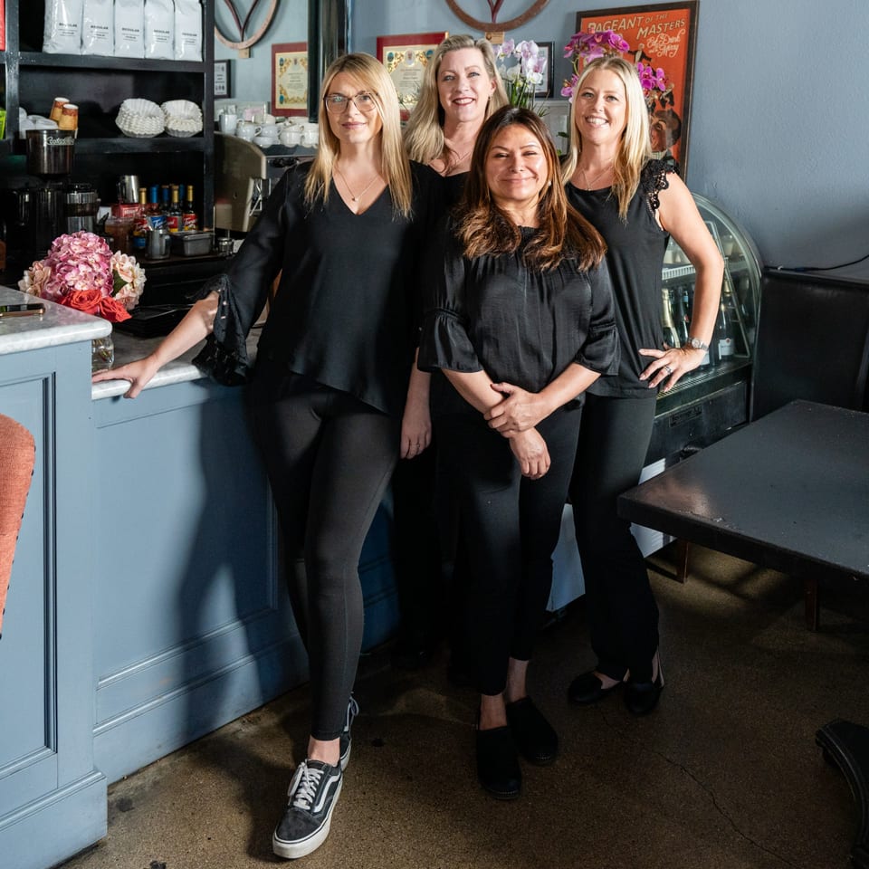 Four smiling women in black shirts and pants stand together inside The Bistro K restaurant.