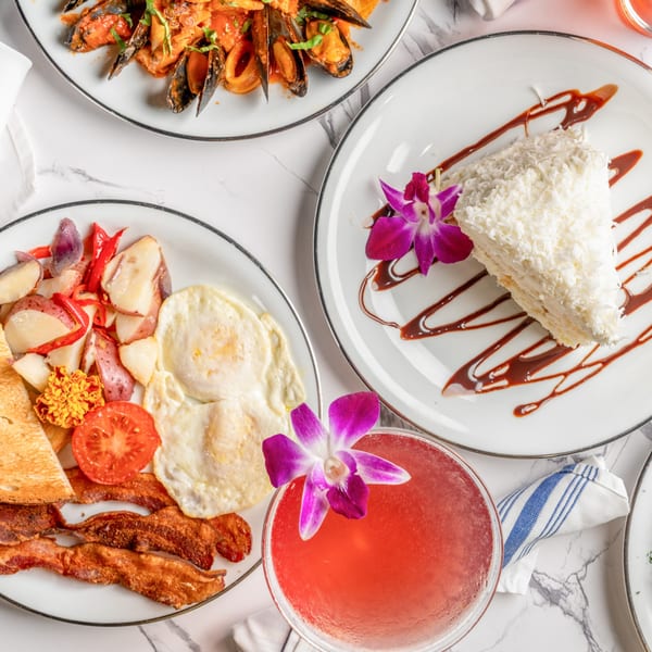 Overhead view of Italian mussels, breakfast plate with bacon and eggs, coconut cake, and a pink cocktail.