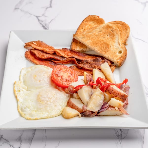 A breakfast plate with crispy bacon, fried eggs, roasted potatoes, grilled tomato, and toast.