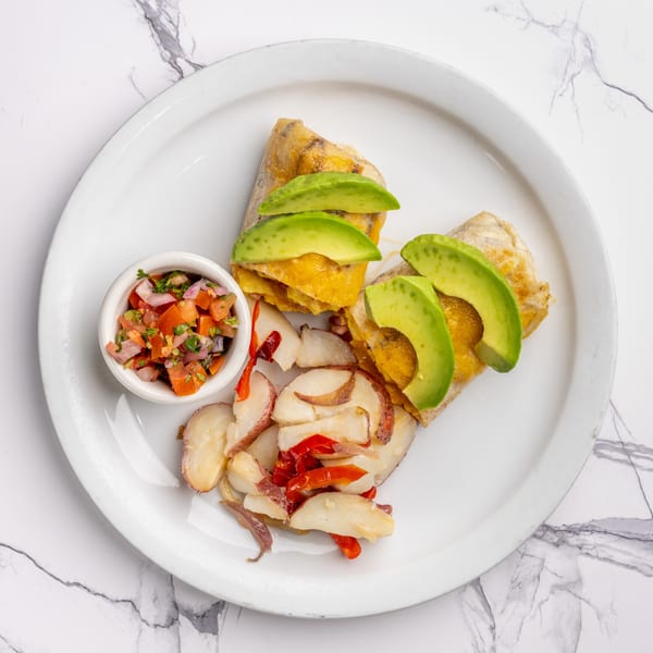 Two breakfast burritos topped with avocado slices, served with roasted potatoes and salsa.