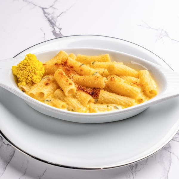 Baked rigatoni pasta with a creamy cheese sauce, breadcrumbs, and a yellow flower garnish.