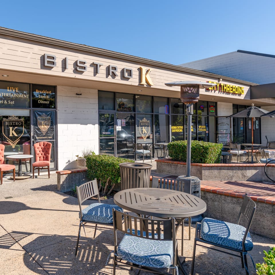 The Bistro K restaurant exterior with outdoor seating, umbrellas, and a patio heater on a sunny day.