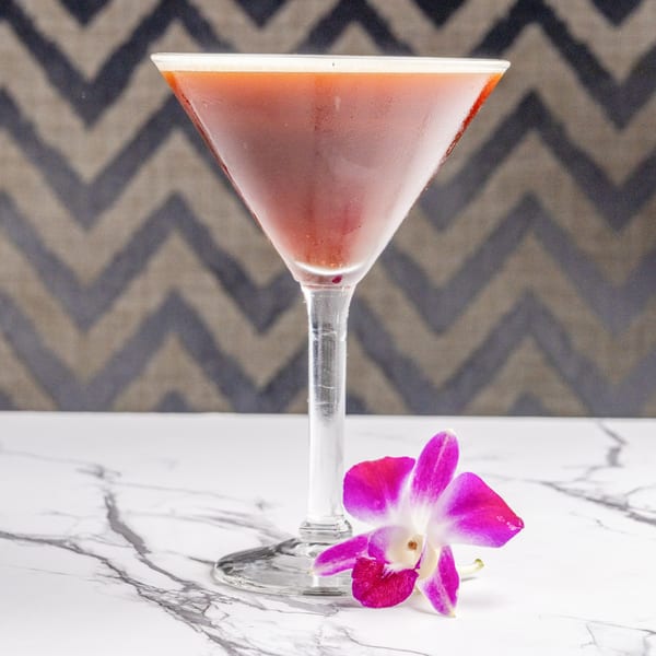 A red martini in a glass with a pink orchid on a marble table at The Bistro K.