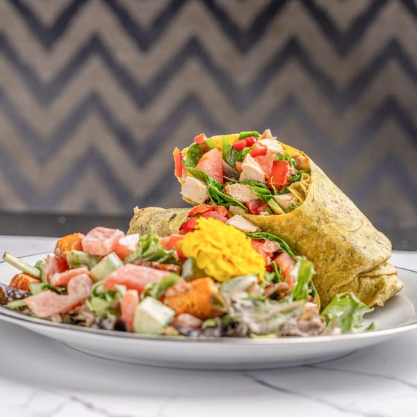 Chicken and vegetable wrap with a side salad, garnished with an edible yellow flower.