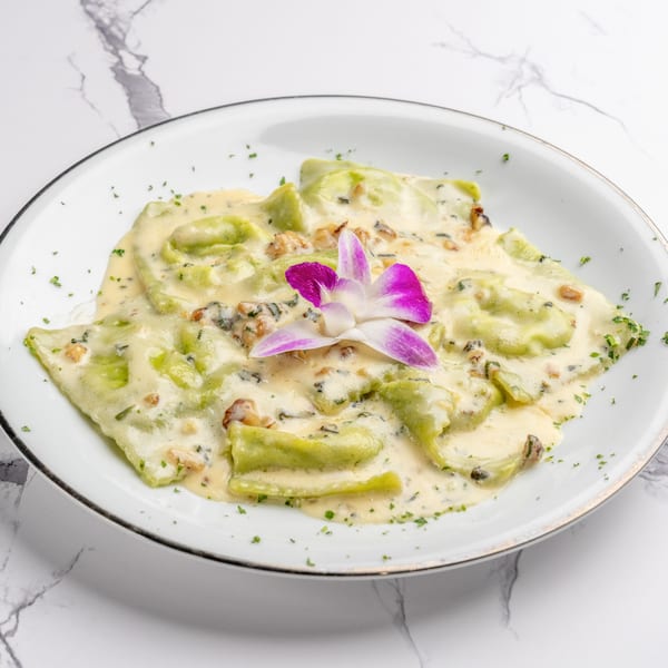 Green ravioli in a creamy sauce, garnished with a purple orchid, on a white plate.