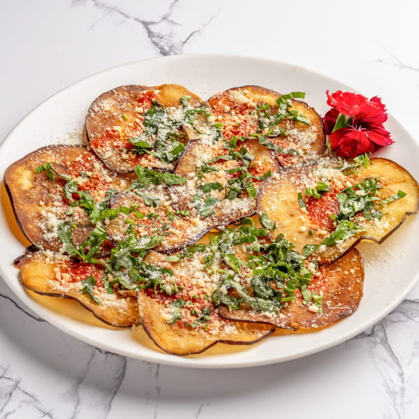 Italian eggplant parmesan slices with tomato sauce, cheese, and basil, garnished with a red flower.