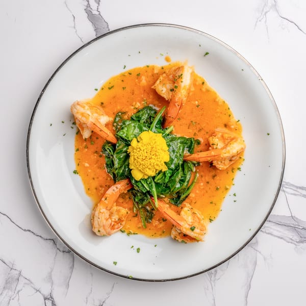 Shrimp in orange sauce with spinach and a yellow edible flower on a white plate.