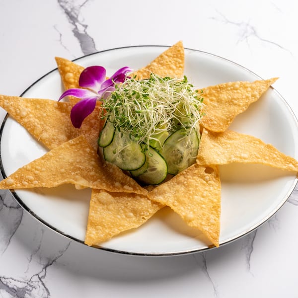Crispy wonton triangles surround a mound of cucumber slices and sprouts, garnished with a purple orchid.