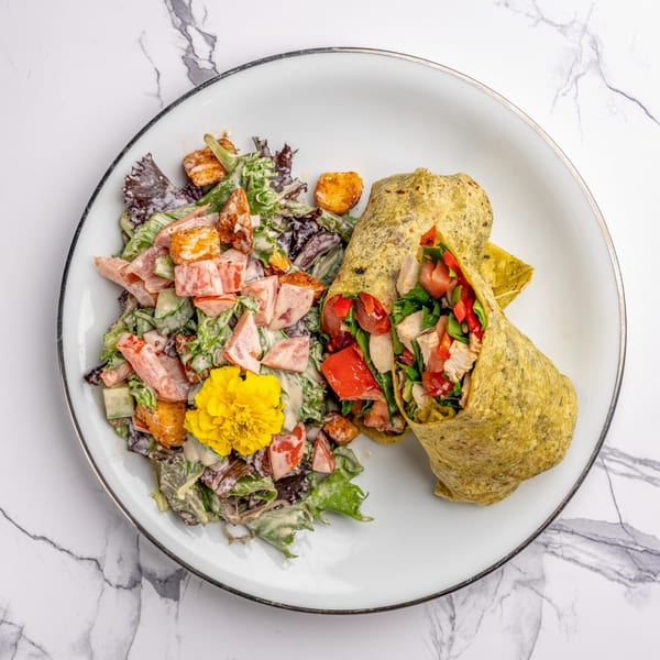 A chicken wrap with red peppers and lettuce, served with a side salad and yellow flower.