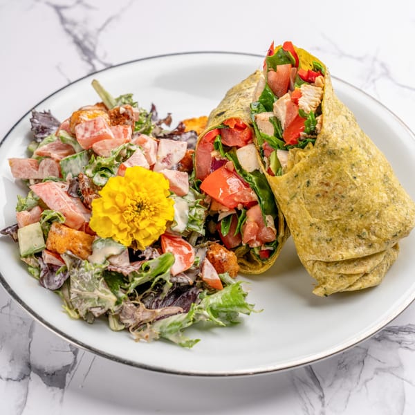 A chicken wrap with tomatoes and spinach, served with a side salad topped with a yellow flower.