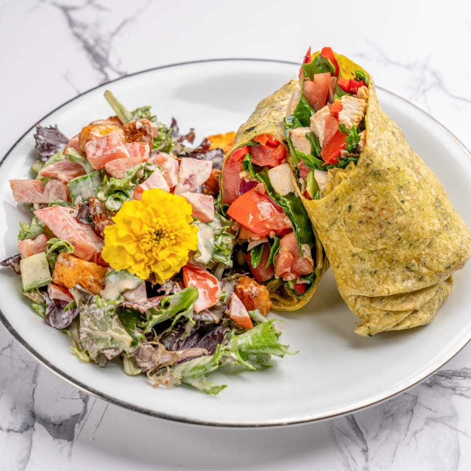 A chicken wrap with tomatoes and spinach, served with a side salad topped with a yellow flower.