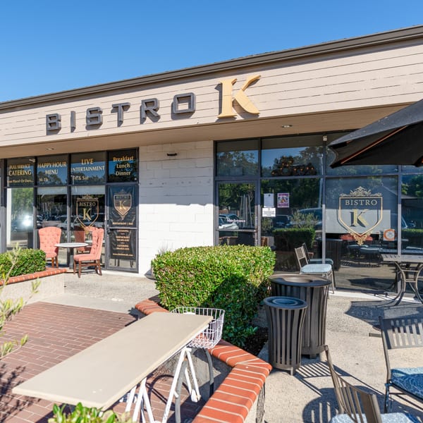 The Bistro K storefront with outdoor seating, large windows, and a clear blue sky.