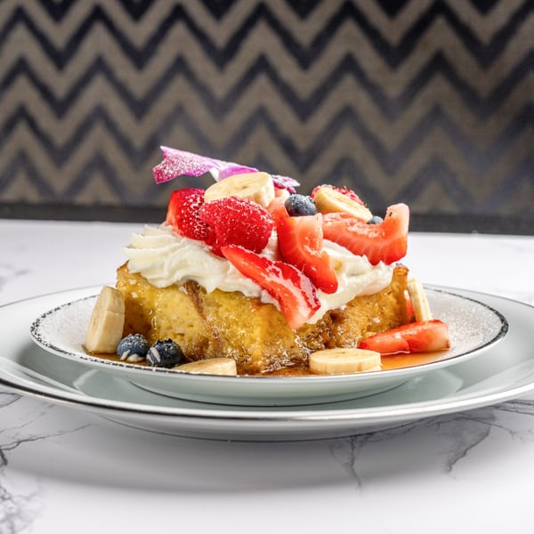 Golden French toast topped with whipped cream, strawberries, blueberries, and banana slices.