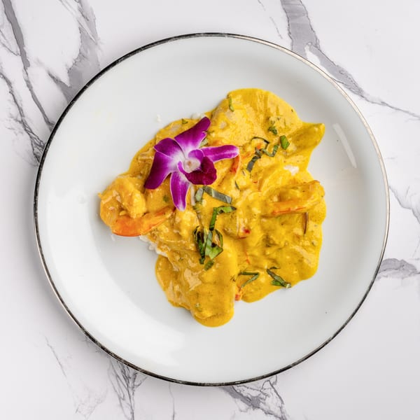 Shrimp in a rich yellow curry sauce, garnished with a purple orchid and fresh herbs.