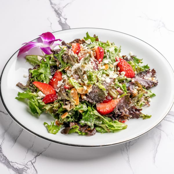 A vibrant Italian salad with mixed greens, strawberries, feta cheese, and nuts, garnished with an orchid.