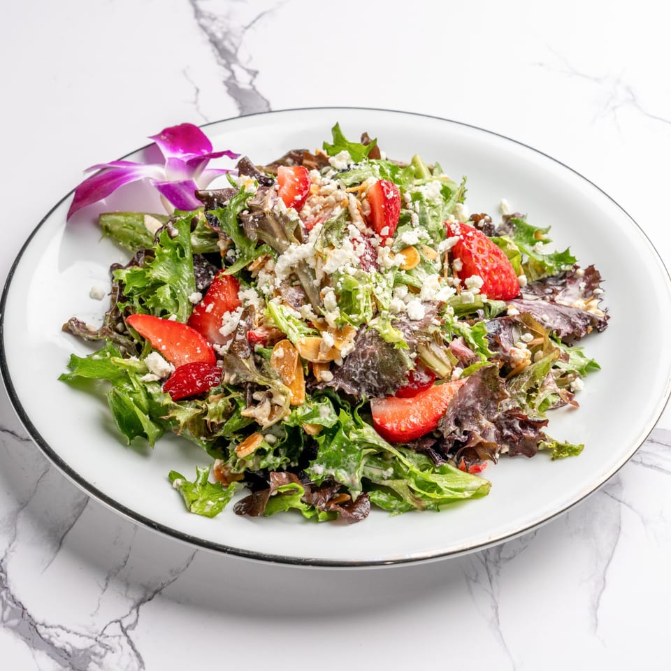 A vibrant Italian salad with mixed greens, strawberries, feta cheese, and nuts, garnished with an orchid.