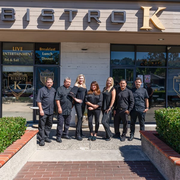 Seven Bistro K staff members, dressed in black, stand smiling outside the restaurant's entrance.