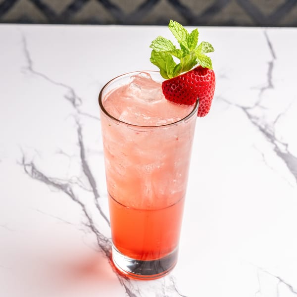 A refreshing strawberry cocktail with mint garnish and ice, served in a tall glass on a marble surface.