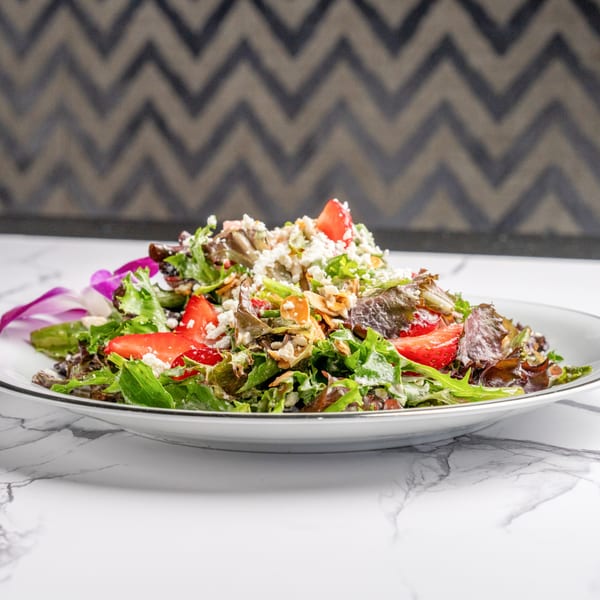 A vibrant Italian salad with mixed greens, strawberries, feta cheese, and almonds on a white plate.