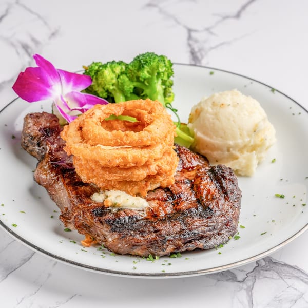 Grilled steak topped with onion rings and butter, served with mashed potatoes and broccoli.