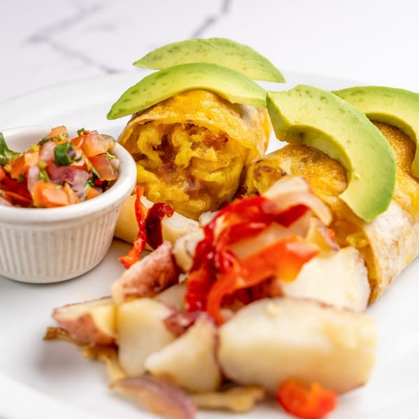 Two breakfast burritos topped with avocado slices, served with salsa and roasted potatoes.