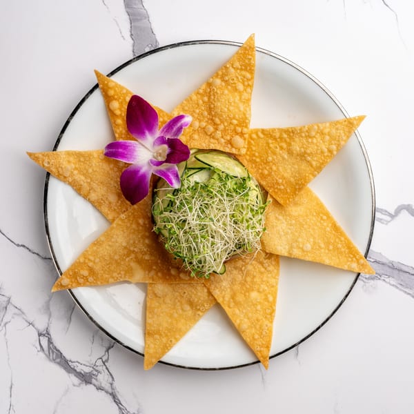 Crispy wonton triangles arranged around a bowl of sprouts and cucumber, garnished with an orchid.