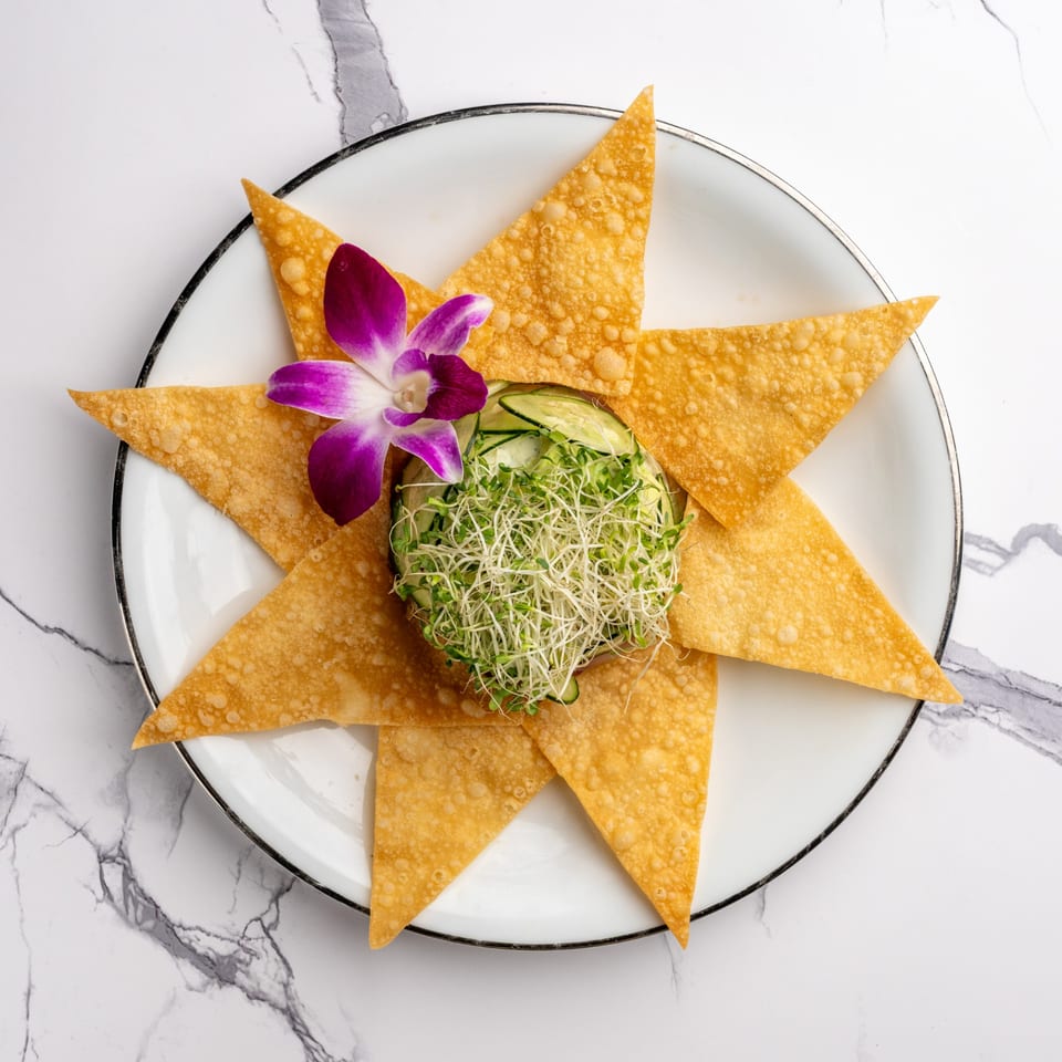 Crispy wonton triangles arranged around a bowl of sprouts and cucumber, garnished with an orchid.