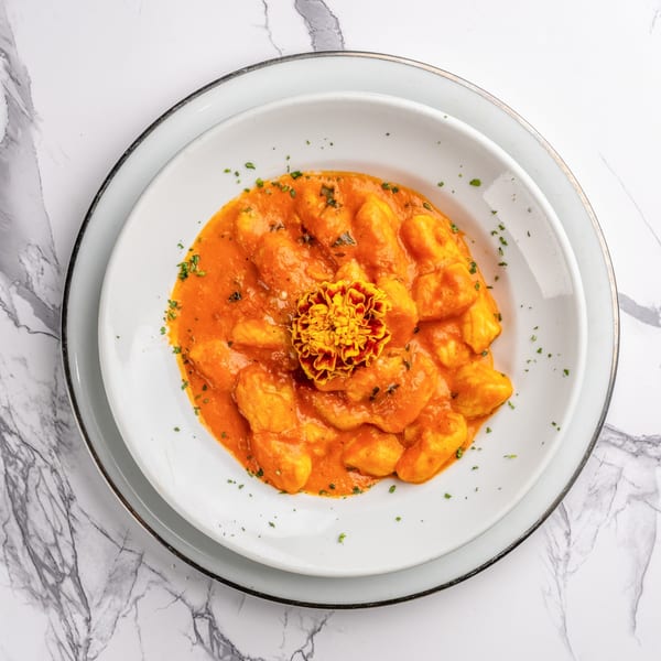Gnocchi in a creamy orange sauce, garnished with parsley and an edible flower, on a white plate.