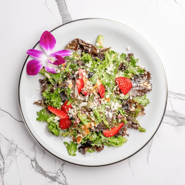 Fresh Italian salad with mixed greens, strawberries, feta cheese, and almonds, garnished with an orchid.