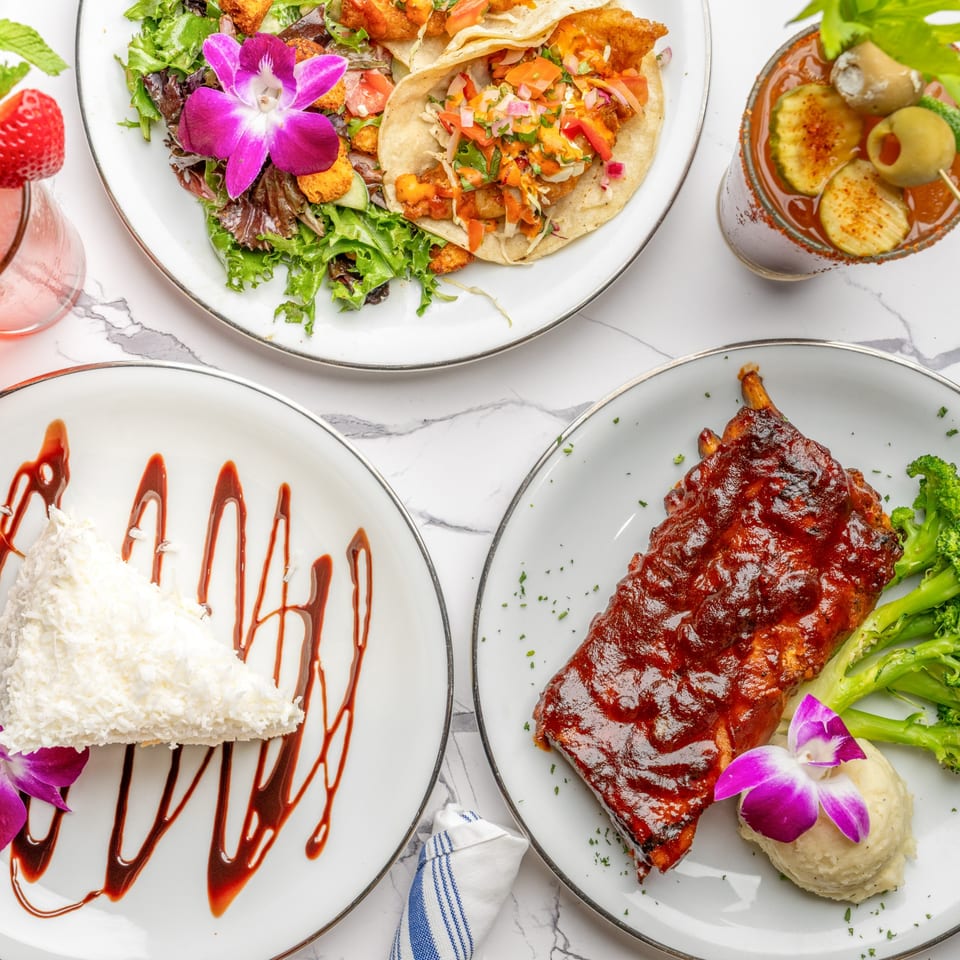 An overhead shot of The Bistro K's Italian dishes, including tacos, ribs, cake, and a Bloody Mary.