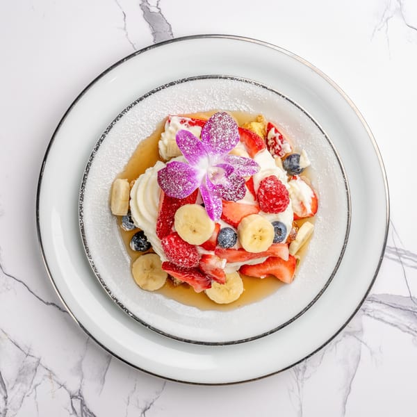 Overhead view of a dessert with whipped cream, mixed berries, banana slices, and a purple orchid.