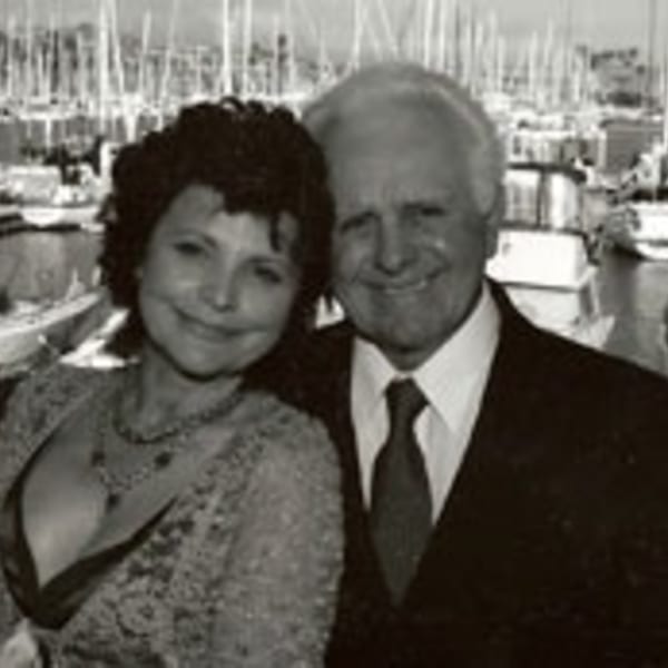 Black and white photo of a smiling couple with a marina full of boats in the background.