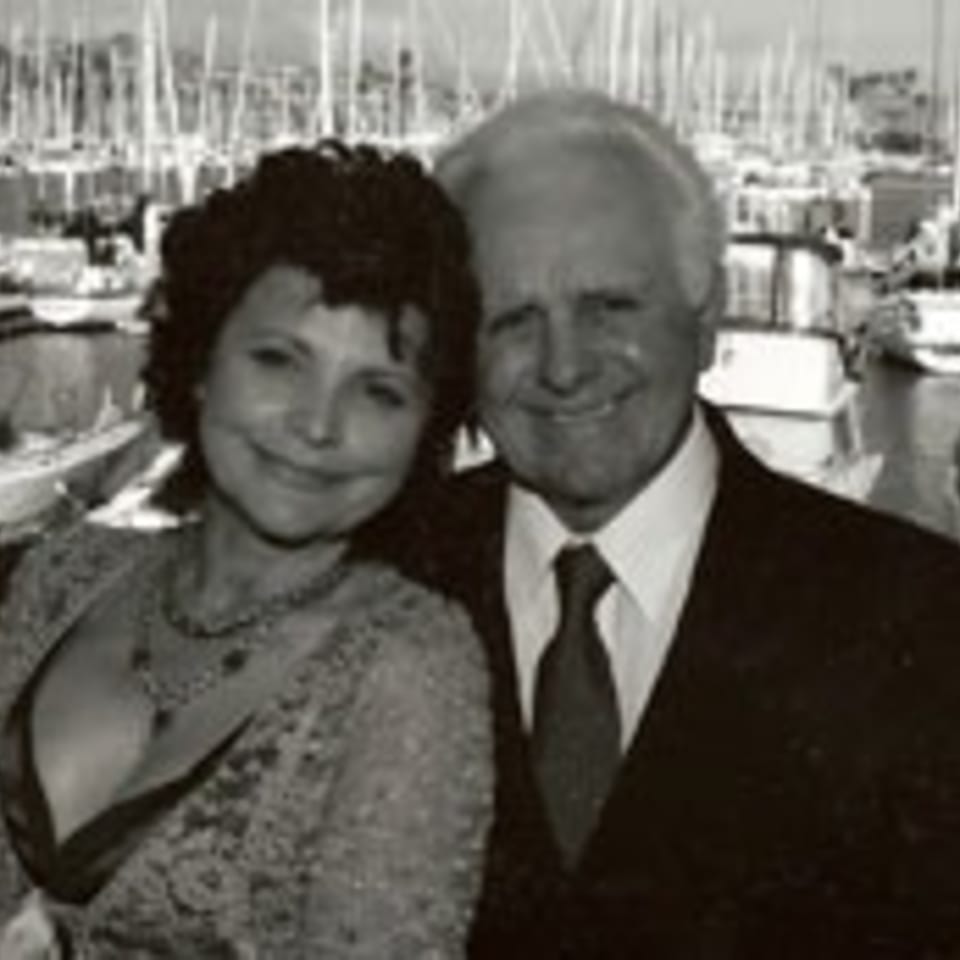Black and white photo of a smiling couple with a marina full of boats in the background.